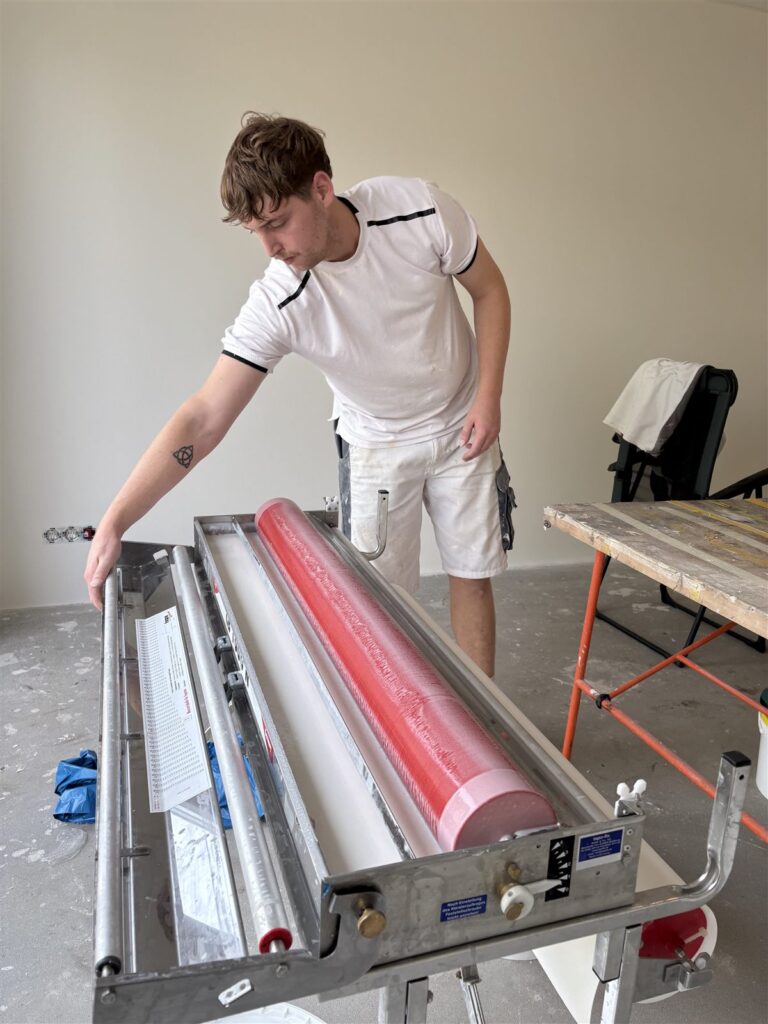 Behanger trekt een ingelijmde baan glasvlies uit de lijmmachine