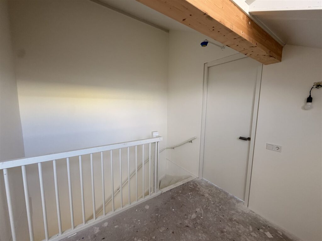 Overloop met trapgat en strak afgewerkte witte wanden onder een houten balk