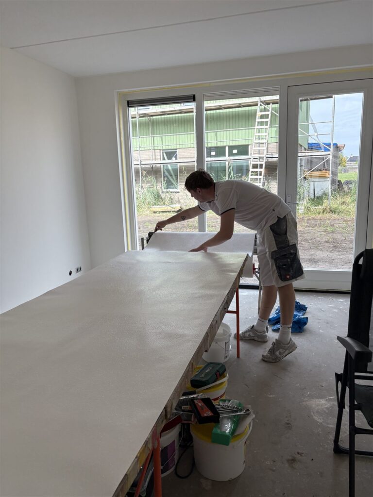 Lange plaktafel in een lege nieuwbouwkamer, waar de banen glasvlies op maat worden gemaakt