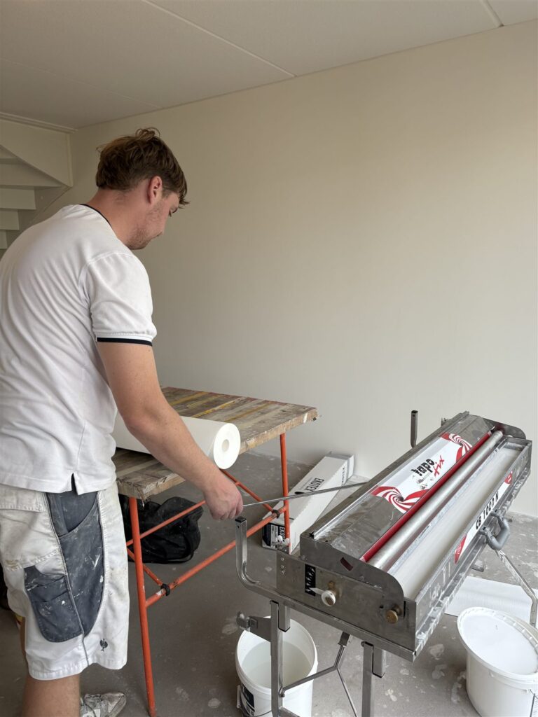 Behanger bereidt de lijmmachine en de plaktafel voor in een lege nieuwbouwwoning