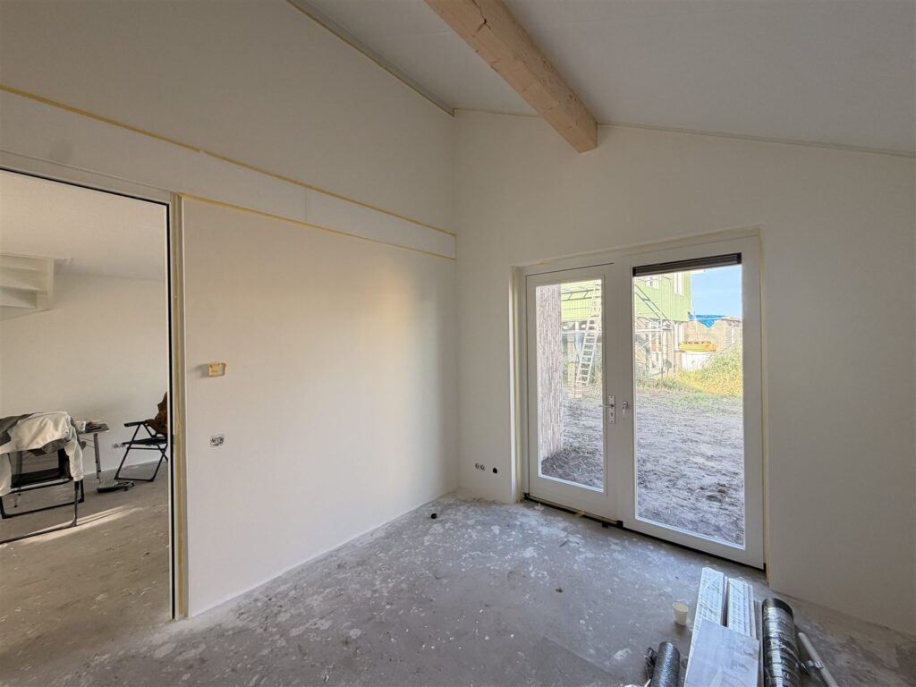 Ruimte met tuindeuren en strakke witte wanden onder een houten balk